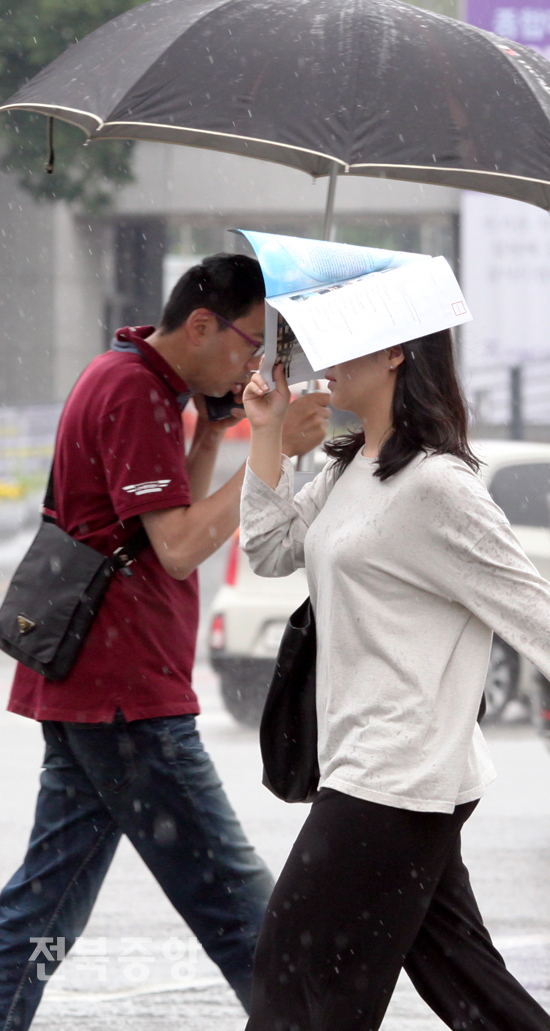 19일 전주시 덕진구 금암동에서 우산을 준비하지 못한 한 여성이 책으로 비를 피하며 신호등을 건너고 있다. /김현표기자
